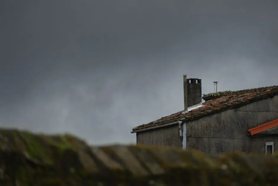 A rustic house roof with chimney under a dramatic, stormy sky.